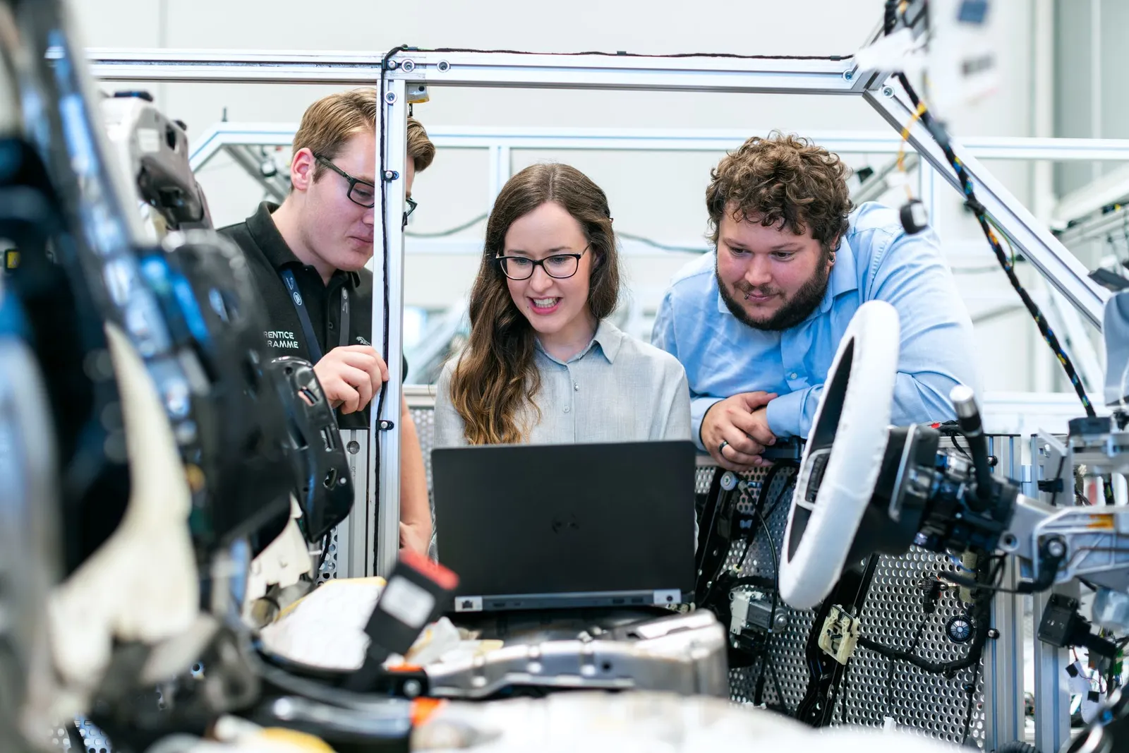Three colleagues looking at a laptop together in an assembly workshop