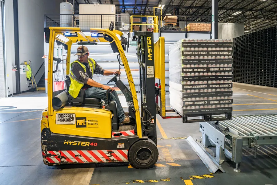 Forklift driver lifting a pallet of canned goods onto a conveyor in a warehouse